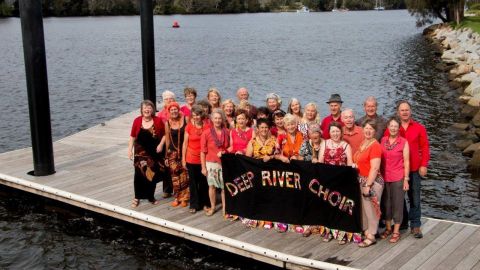 Group of people wearing red shirts standing together on a jetty with water in the background