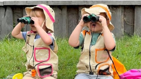 Two children sitting next to each other on the grass holding binoculars