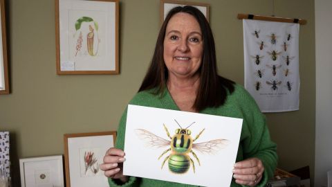 A woman holding a painting of a bee.