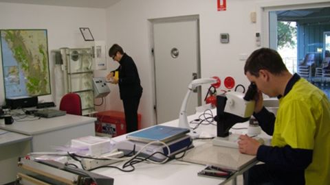 A man looking through a microscope and a woman packing seeds away in an office.